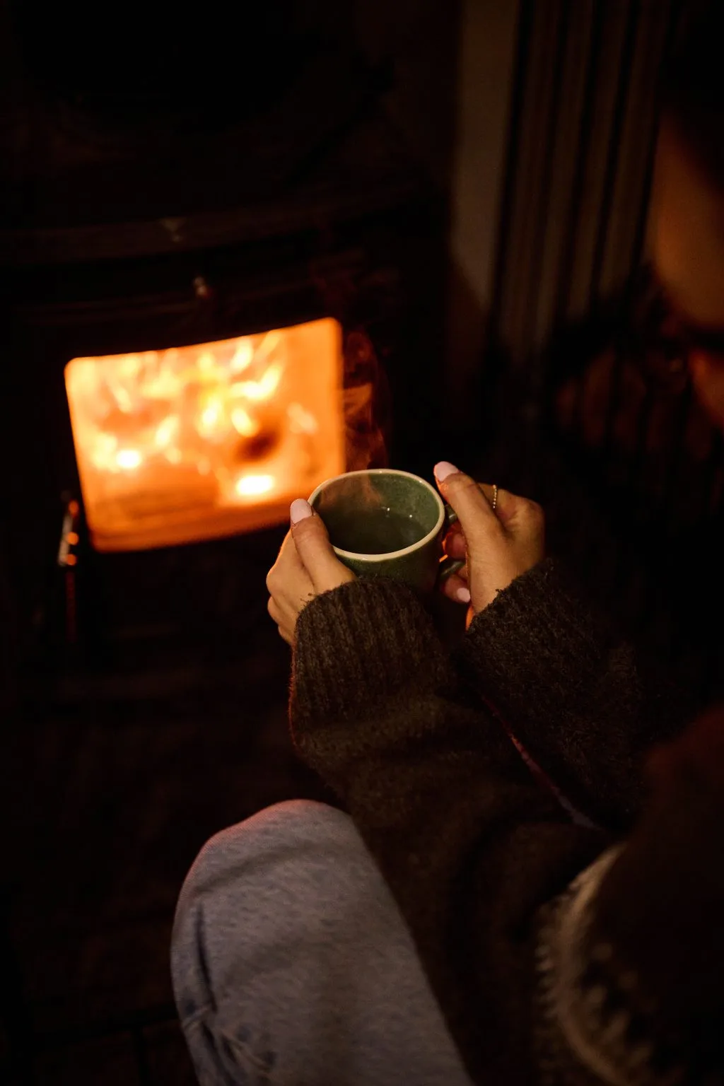 A hand holding a mug in front of a glowing wood burner