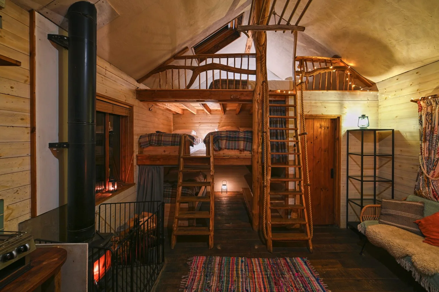 Inside a Tree Lodge, with a wood burner and a ladder to a sleeping loft
