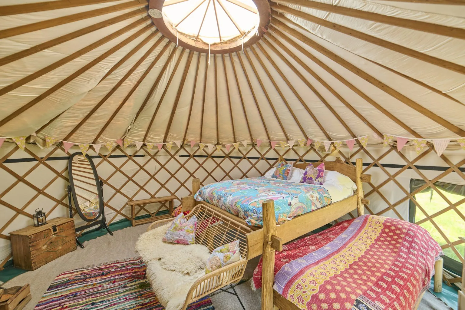 Inside a Meadow Yurt, with a bed made up beneath the wooden lattice roof