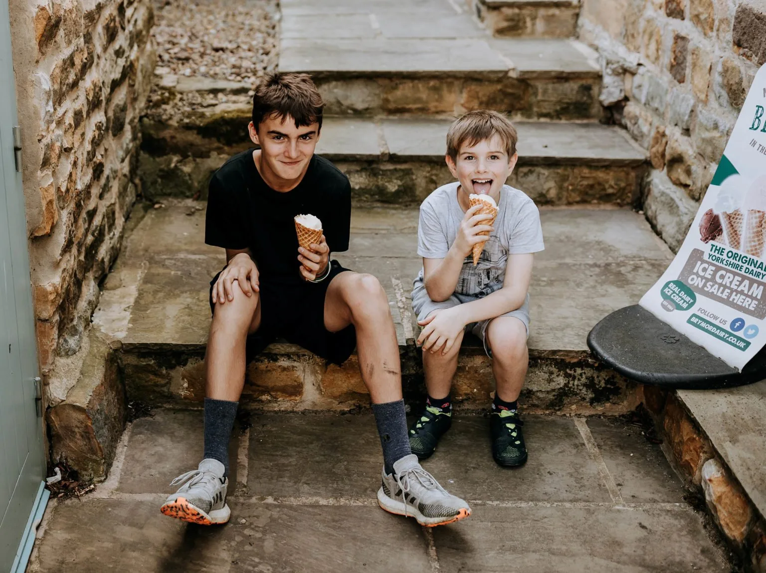 Two children eating ice cream on a stone step during a family stay