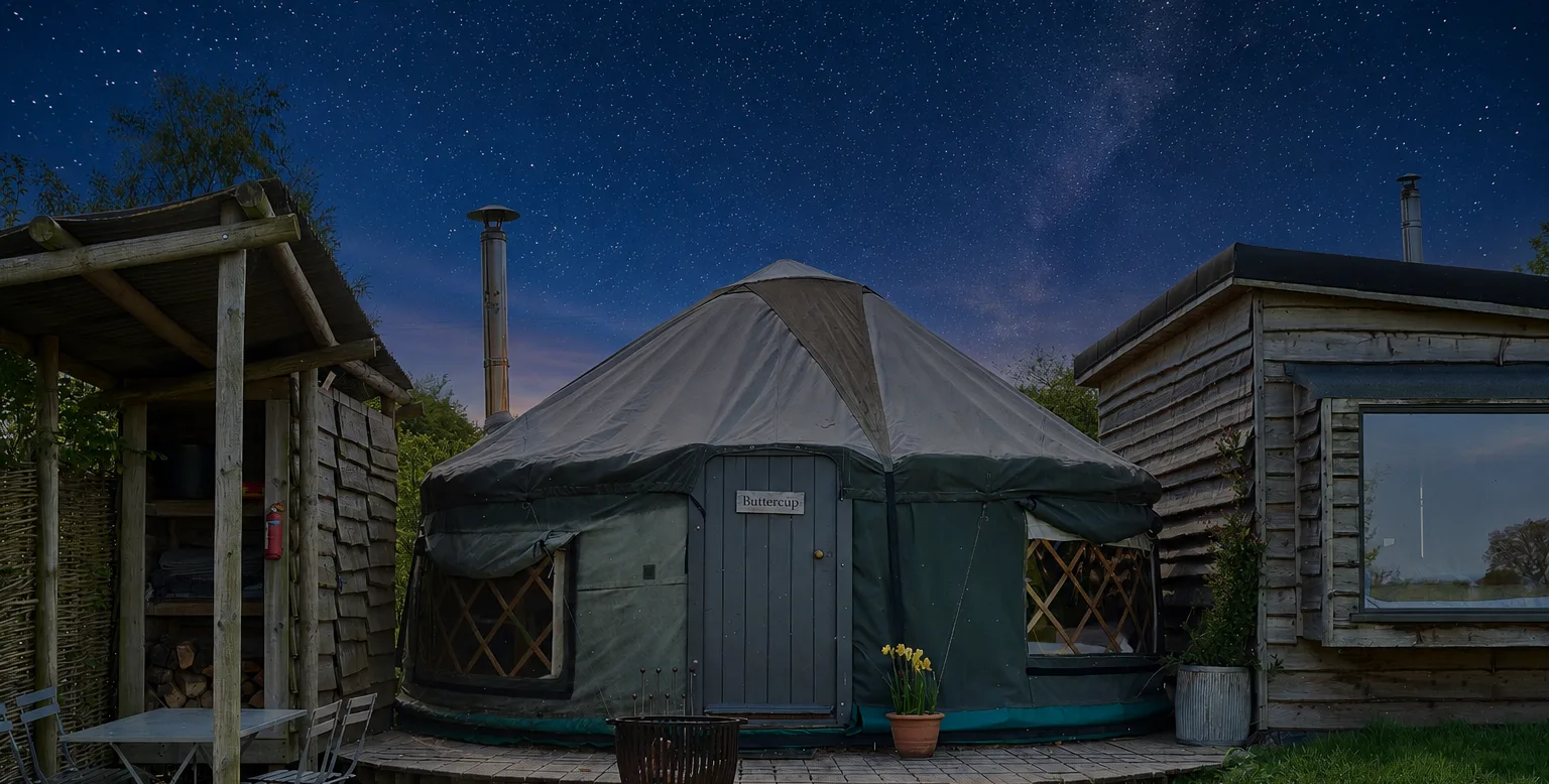 A Cabin Yurt at Swinton Bivouac glowing under a night sky, with a wood burner flue beside it
